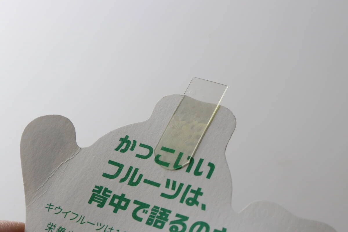 「かっこいいフルーツは、背中で語るのさ」と書かれたカードの裏面に透明な伸びるテープを貼っている 「かっこいいフルーツは、背中で語るのさ」と書かれたカードの裏面に透明な伸びるテープを貼っている