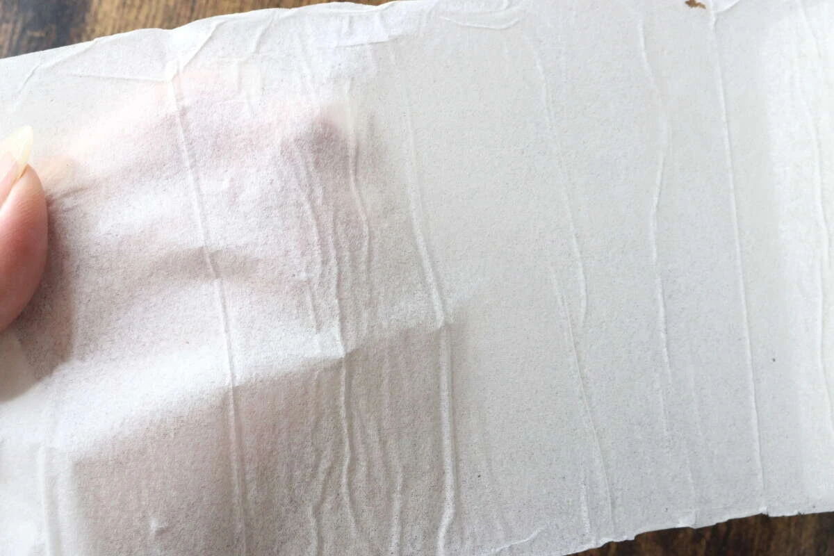 指で広げられた圧縮トイレットペーパーの紙が薄く透けている様子。 指で広げられた圧縮トイレットペーパーの紙が薄く透けている様子。