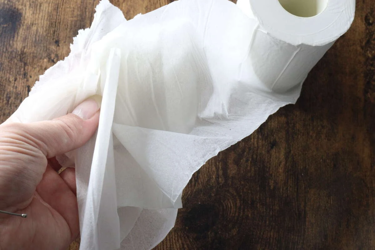 指で圧縮トイレットペーパーの紙を重ねて持ち、柔らかさを確認している様子。 指で圧縮トイレットペーパーの紙を重ねて持ち、柔らかさを確認している様子。