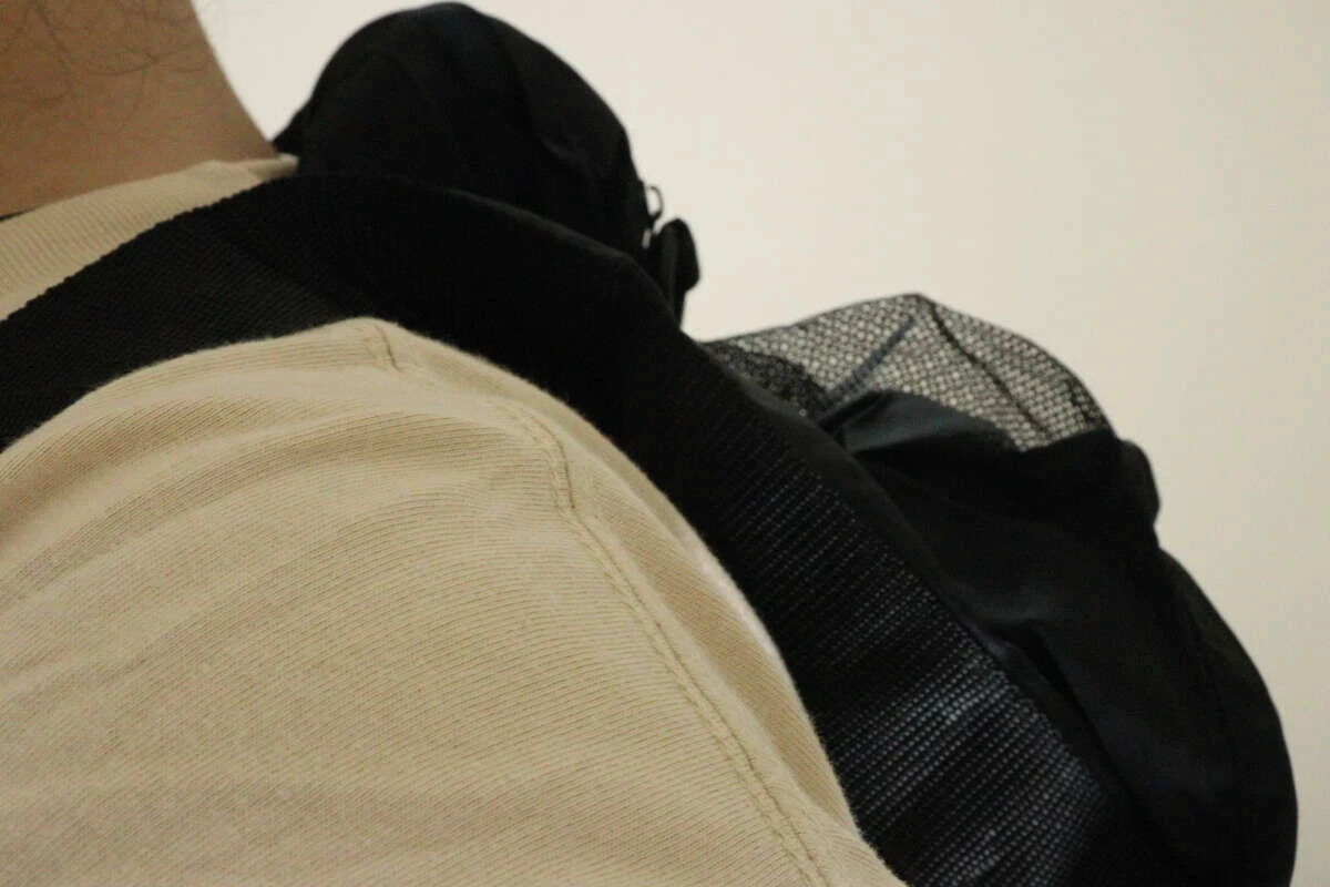 ベージュのTシャツを着た人が黒いバッグをリュックのように背負っている肩越しのアングル