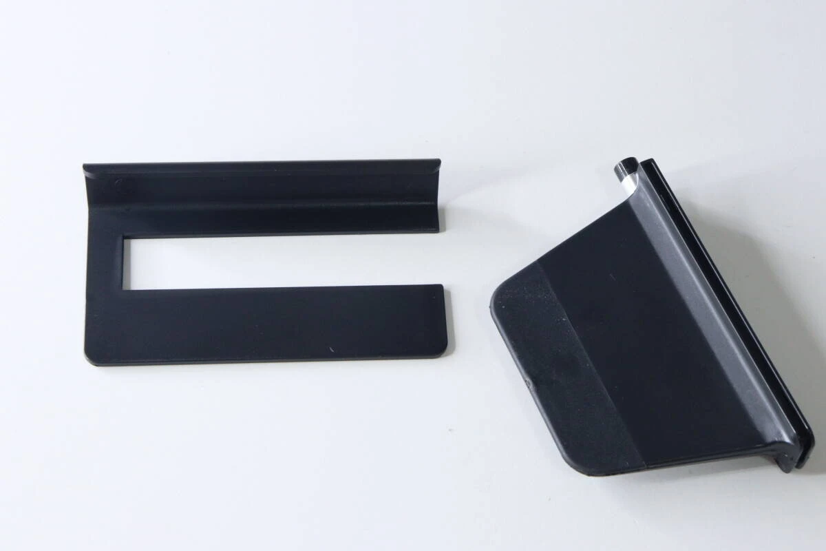 白い背景に置かれた、分解された状態の黒いスマホスタンドのパーツ2つ。 白い背景に置かれた、分解された状態の黒いスマホスタンドのパーツ2つ。