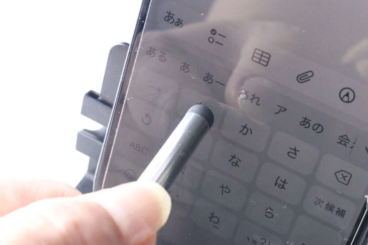 銀色のタッチペンを使って、スマートフォン画面のキーボードを操作している様子。 銀色のタッチペンを使って、スマートフォン画面のキーボードを操作している様子。