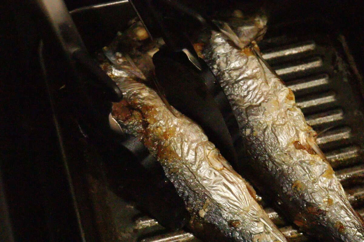グリルで焼かれた焼き魚をシリコーントングで掴んでいる グリルで焼かれた焼き魚をシリコーントングで掴んでいる