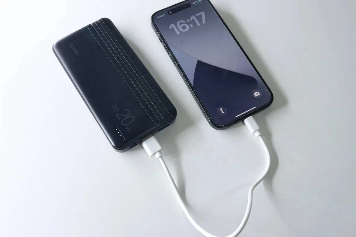 黒いモバイルバッテリーとスマートフォンが白い充電ケーブルで接続され充電中 黒いモバイルバッテリーとスマートフォンが白い充電ケーブルで接続され充電中