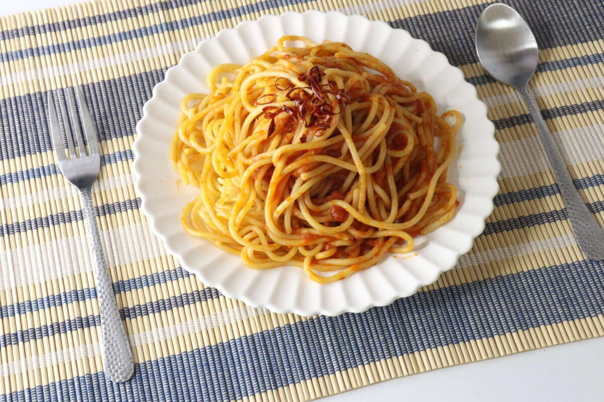 トマトソースのパスタが盛られた白い皿の左右に槌目風スプーンとフォークが置かれている トマトソースのパスタが盛られた白い皿の左右に槌目風スプーンとフォークが置かれている