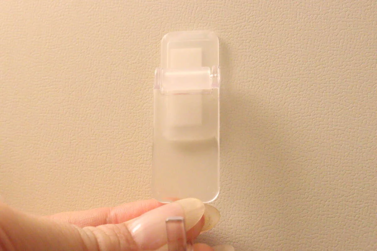 粘着テープを貼り付けた洗面スイングフックを指で持っている様子