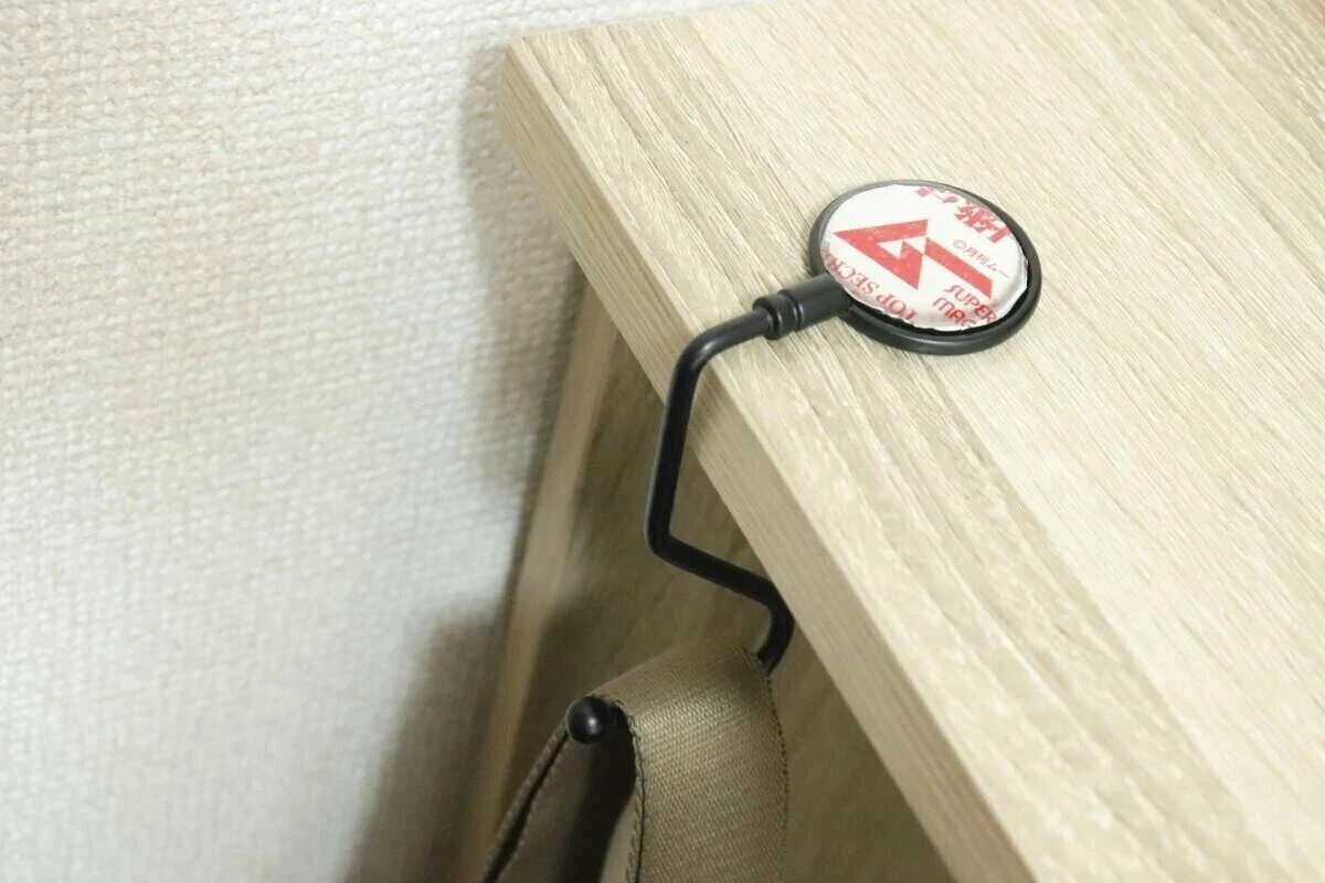 黒いバッグフックが木目調のテーブルの縁に設置され、下にバッグが掛けられている