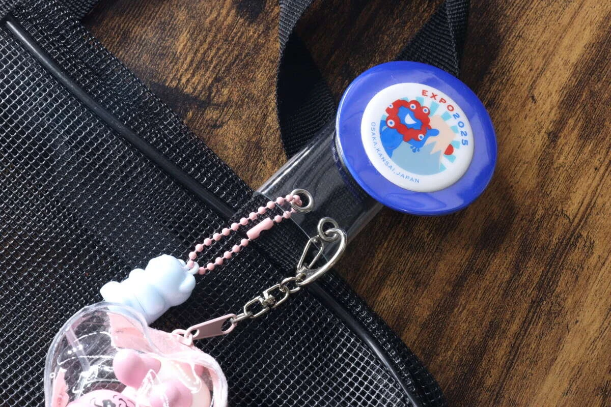 黒いバッグの持ち手に缶バッジとピンクのキーホルダーが装着された様子 黒いバッグの持ち手に缶バッジとピンクのキーホルダーが装着された様子