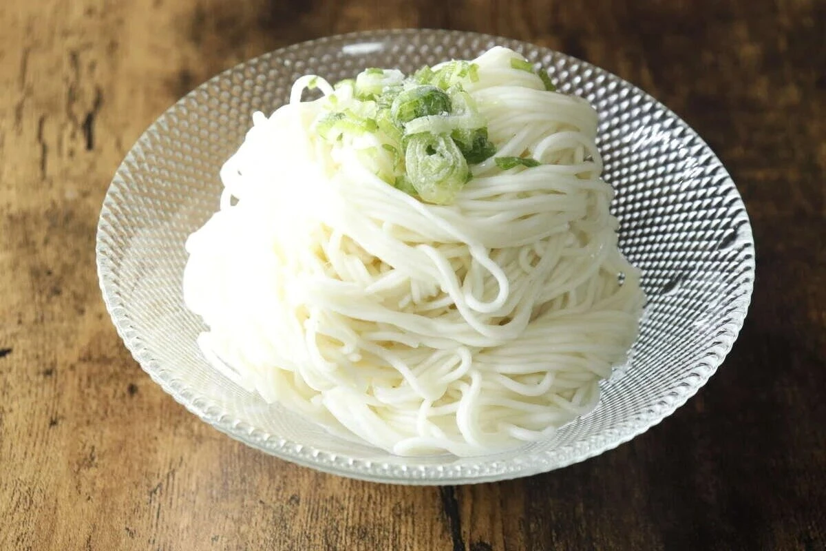 ガラスの器に盛られた冷やしそうめん、刻みネギが乗っている ガラスの器に盛られた冷やしそうめん、刻みネギが乗っている
