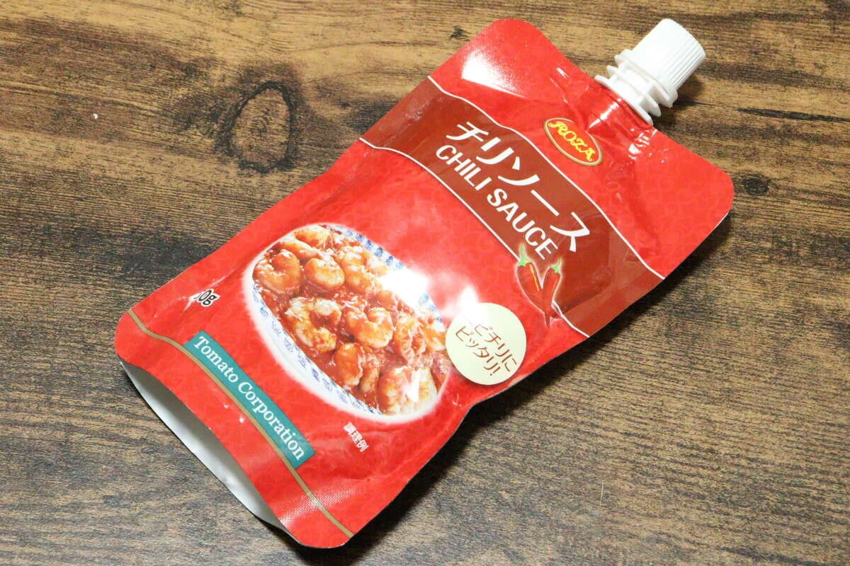 木目のテーブルに斜めに置かれた赤いパウチ容器のチリソース