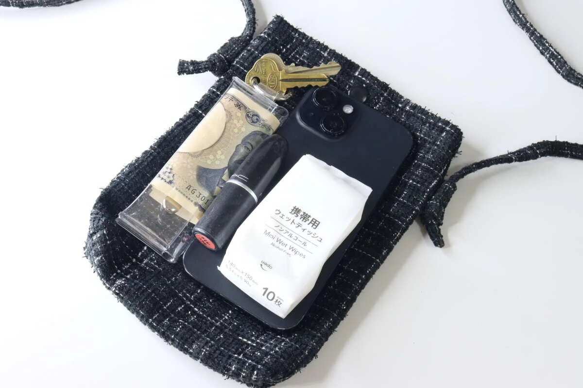 黒いツイードショルダーバッグの中にスマホ、ミニ財布、リップ、鍵、ウェットティッシュが収まっている様子