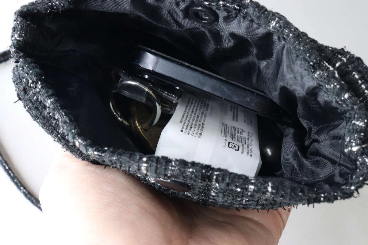 黒いツイードショルダーバッグの中にスマホや鍵などの荷物が入っている様子を上から覗き込んでいる