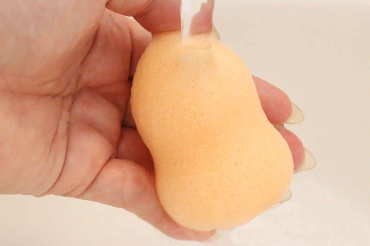 蛇口から流れる水でひょうたん型の洗顔パフを濡らしている手元 蛇口から流れる水でひょうたん型の洗顔パフを濡らしている手元