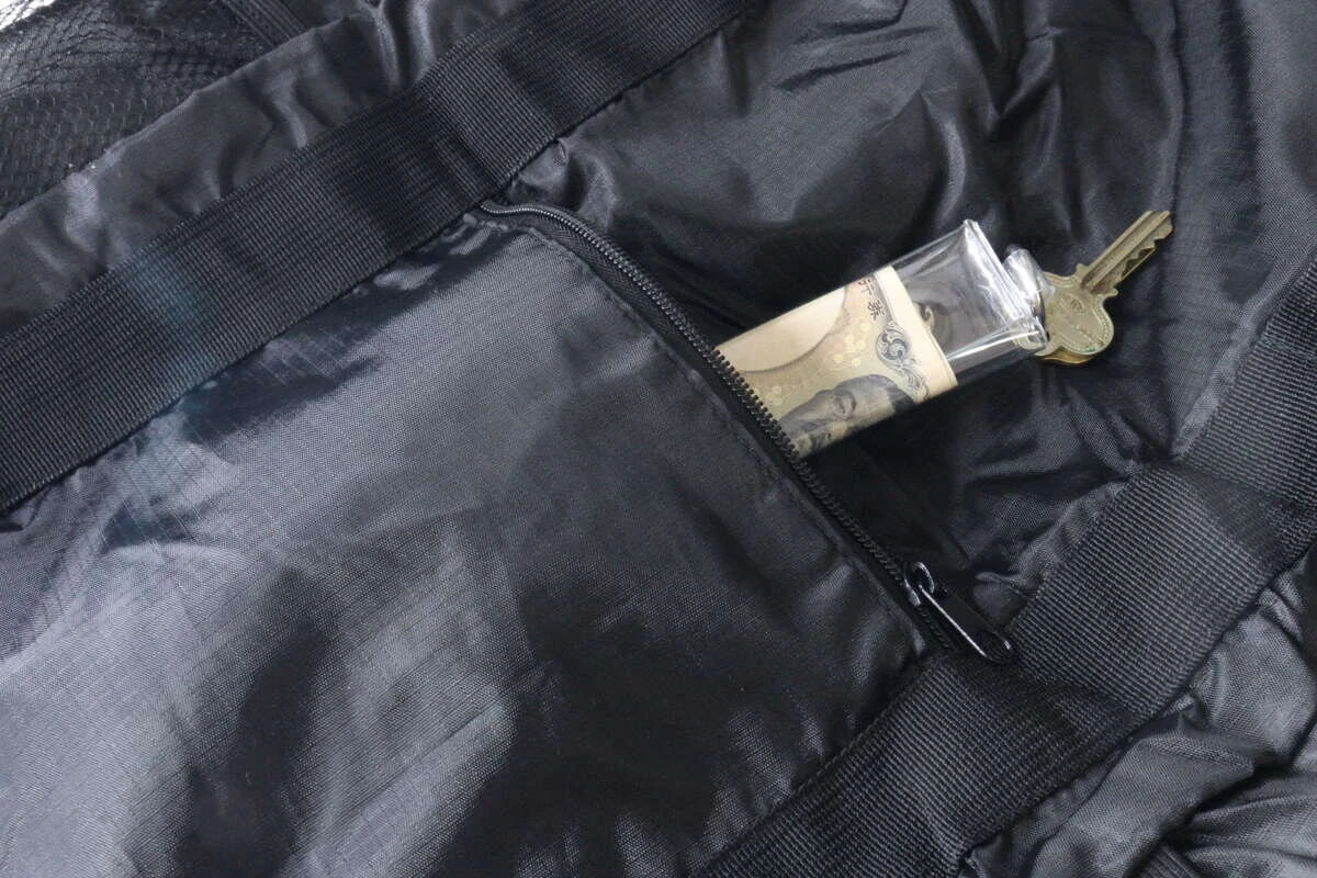 黒いトート型バックパックの前面にあるファスナーポケットに、お札と鍵が入った透明なケースが収納されている。