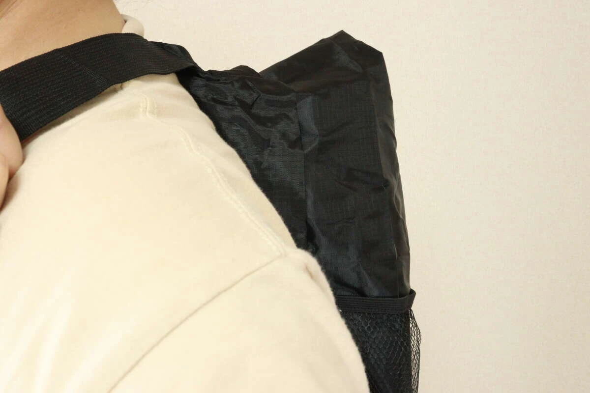 ベージュのシャツを着た人物が、黒いトート型バックパックをバックパックとして背負っている後ろ姿。