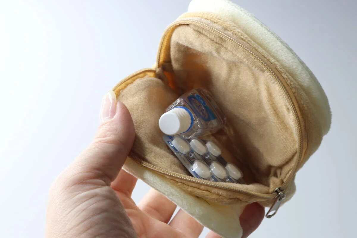 女性の指が食パン型ポーチのファスナーを開け、目薬と錠剤の薬が入っている様子 女性の指が食パン型ポーチのファスナーを開け、目薬と錠剤の薬が入っている様子