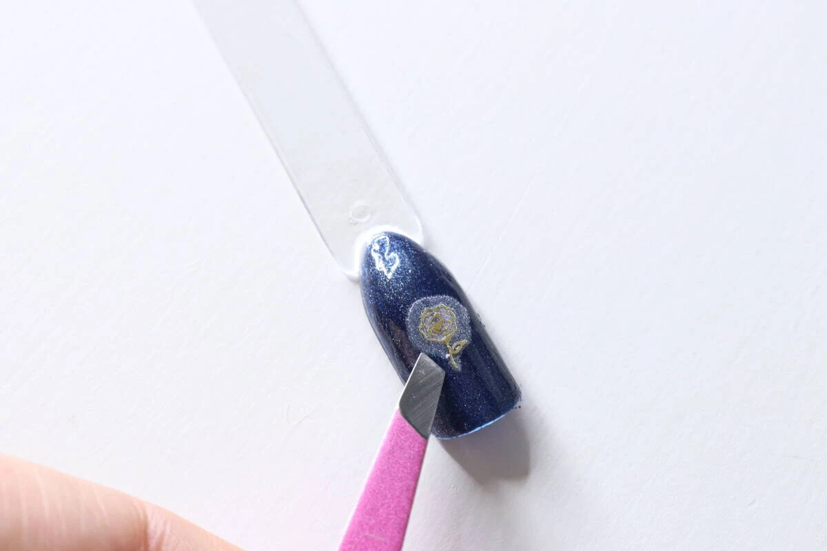 濃いブルーのネイルチップにピンセットを使って薔薇のフィルムを乗せている作業中