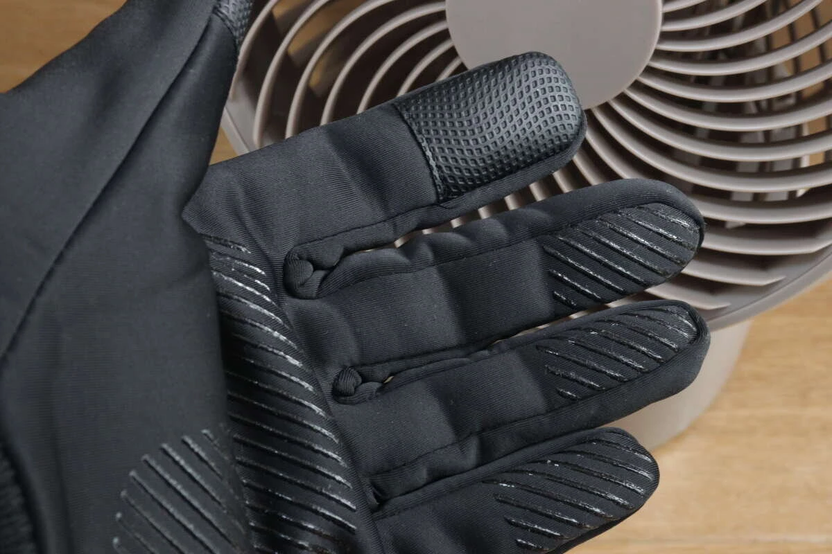 黒い防寒手袋を着用した手のひらをサーキュレーターの前にかざしている様子 黒い防寒手袋を着用した手のひらをサーキュレーターの前にかざしている様子