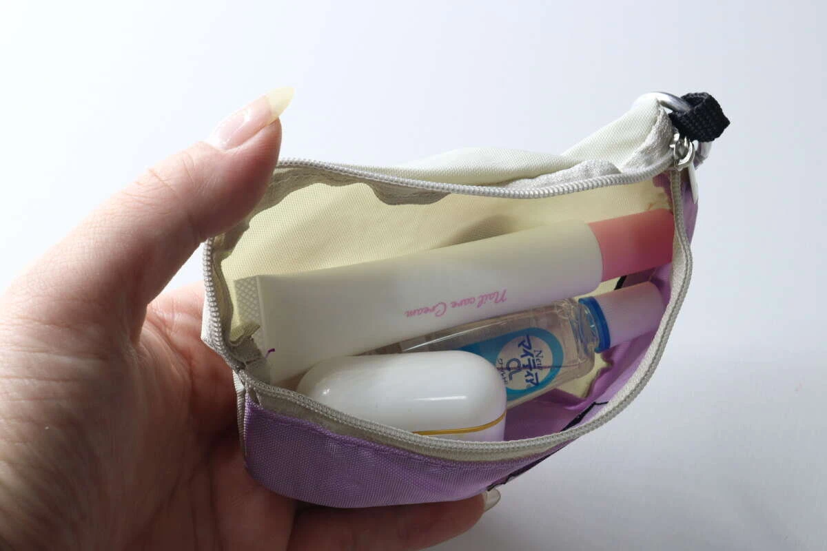女性の手が、ネイルクリームや目薬などの小物をウエストポーチ風キーホルダーに入れている様子 女性の手が、ネイルクリームや目薬などの小物をウエストポーチ風キーホルダーに入れている様子