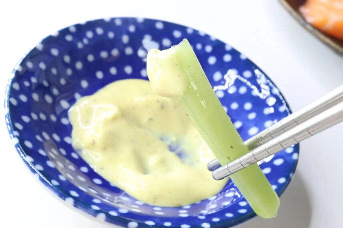 青い小鉢に入ったエリソースに野菜スティックをつけている 青い小鉢に入ったエリソースに野菜スティックをつけている