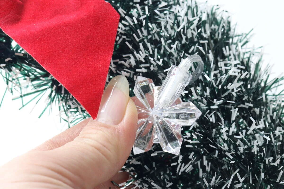クリスマスリースに雪の結晶型のデコレーションライトを組み合わせるため、指で持っている。 クリスマスリースに雪の結晶型のデコレーションライトを組み合わせるため、指で持っている。