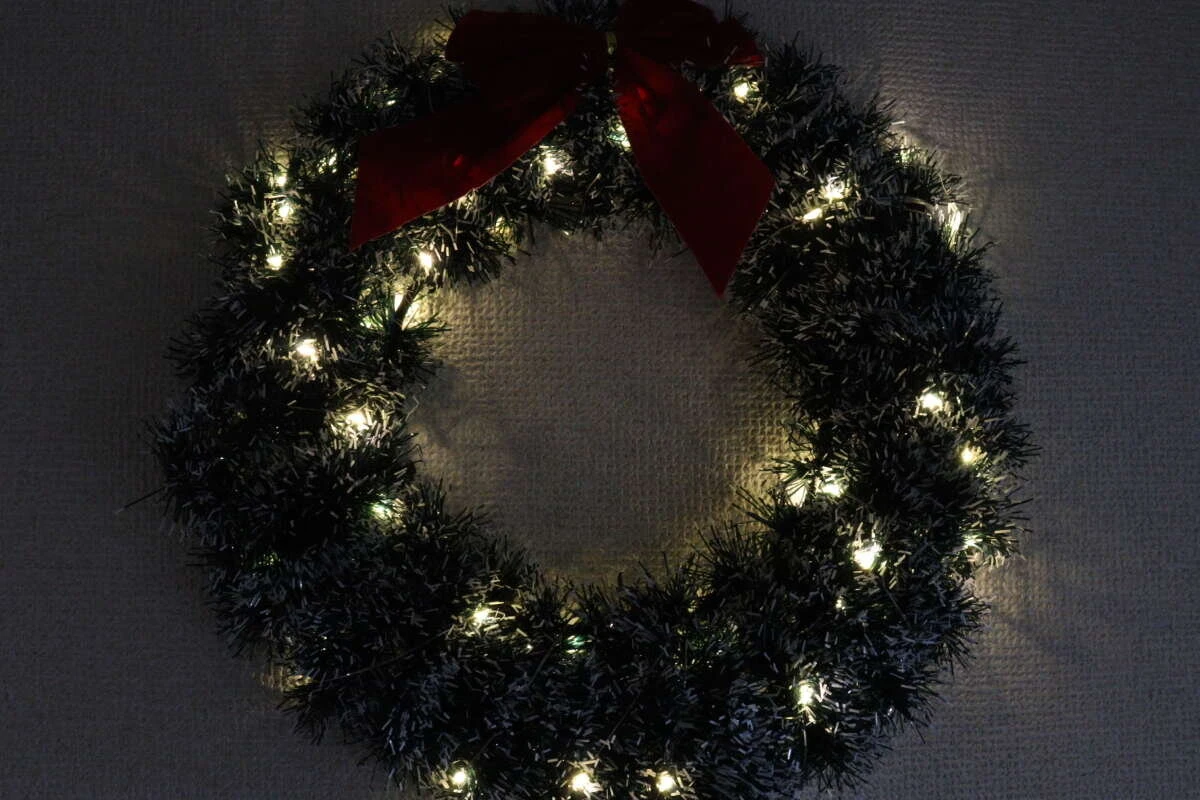 クリスマスリースにストリングライトを巻き付け、暗い部屋で点灯させた様子。 クリスマスリースにストリングライトを巻き付け、暗い部屋で点灯させた様子。