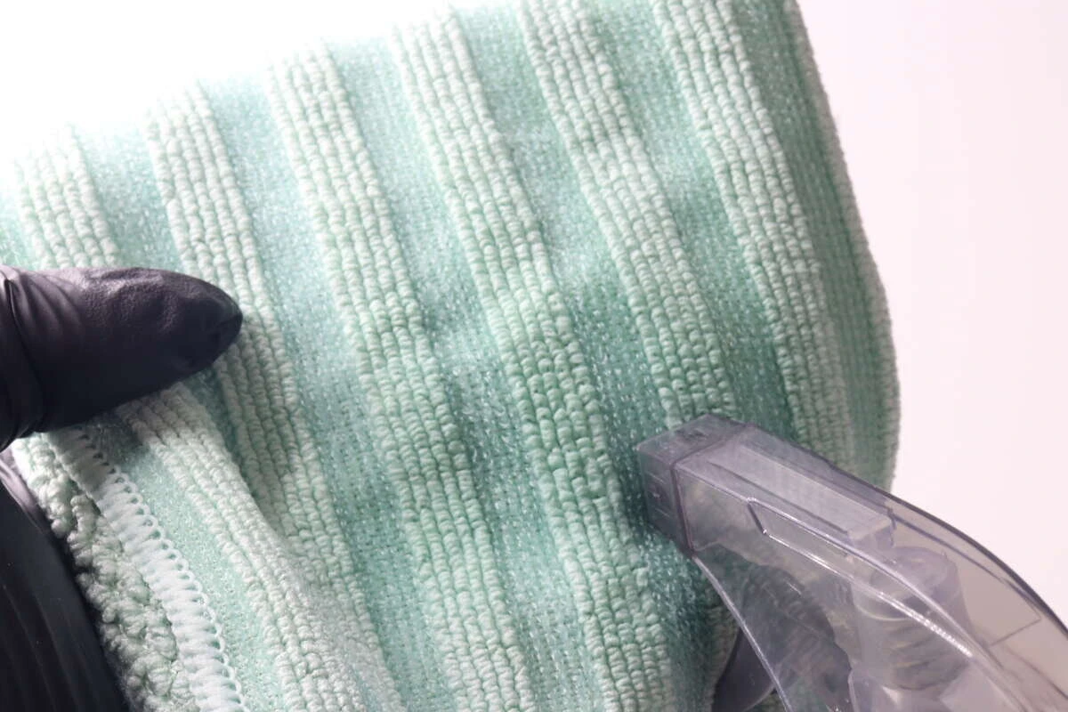 スプレー容器から緑色のマイクロファイバークロスに液を吹き付けている状態