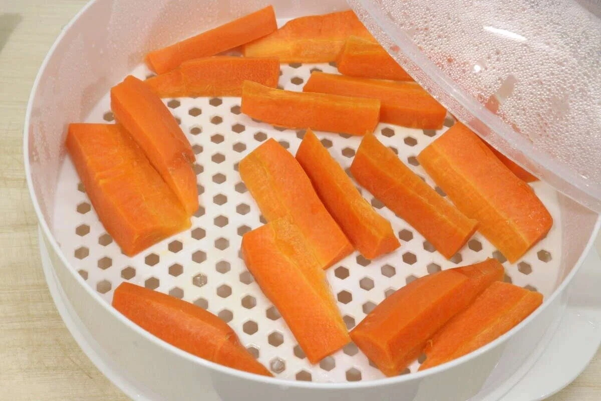 蒸し器のざるの上にスティック状に切られたニンジンが並んでいる状態 蒸し器のざるの上にスティック状に切られたニンジンが並んでいる状態