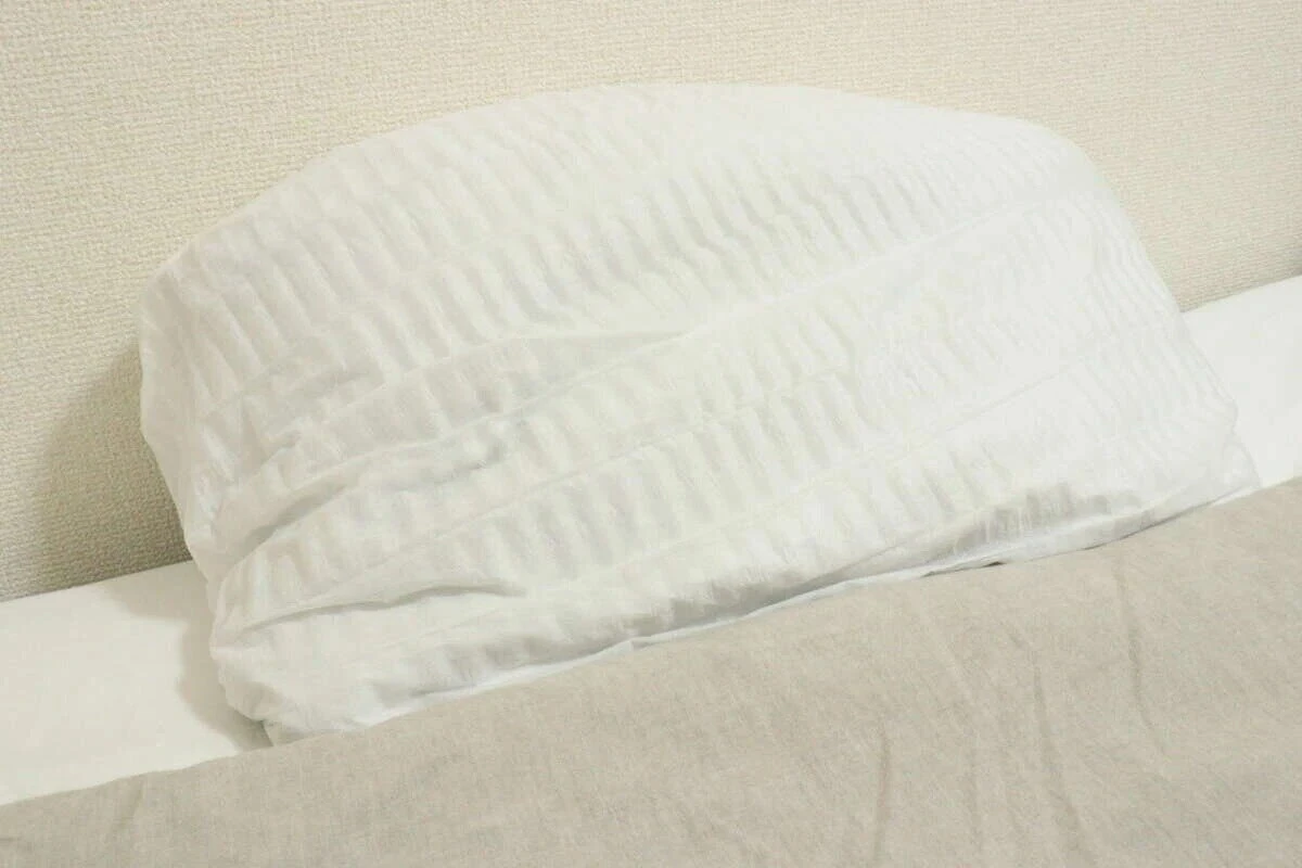 ベッドの上の枕に白い不織布まくらカバーがきれいに装着されている状態を横から撮影したもの ベッドの上の枕に白い不織布まくらカバーがきれいに装着されている状態を横から撮影したもの