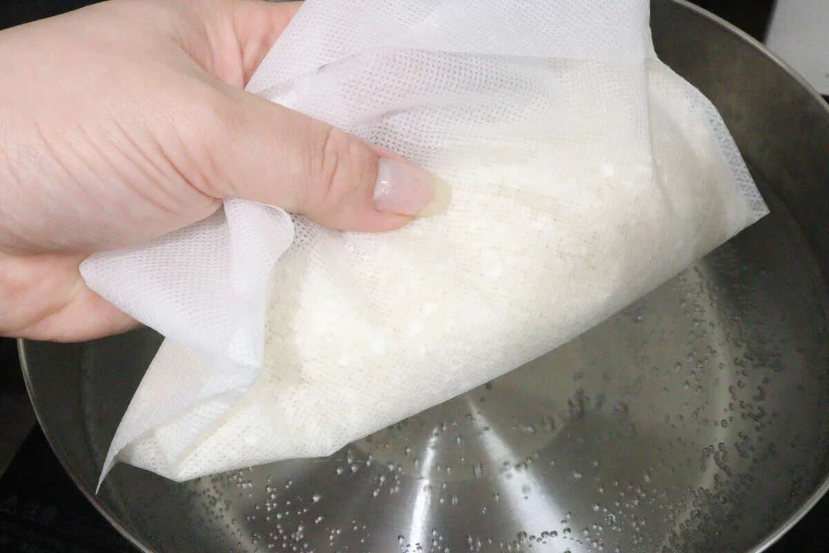沸騰したお湯を入れた鍋に生米を入れた炊飯袋を投入している手元 沸騰したお湯を入れた鍋に生米を入れた炊飯袋を投入している手元