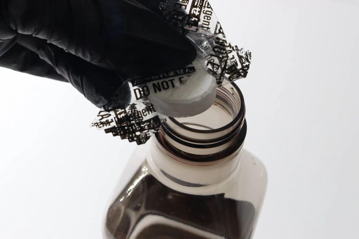 黒い手袋をした手でスプレー容器の口に錠剤を入れている様子 黒い手袋をした手でスプレー容器の口に錠剤を入れている様子