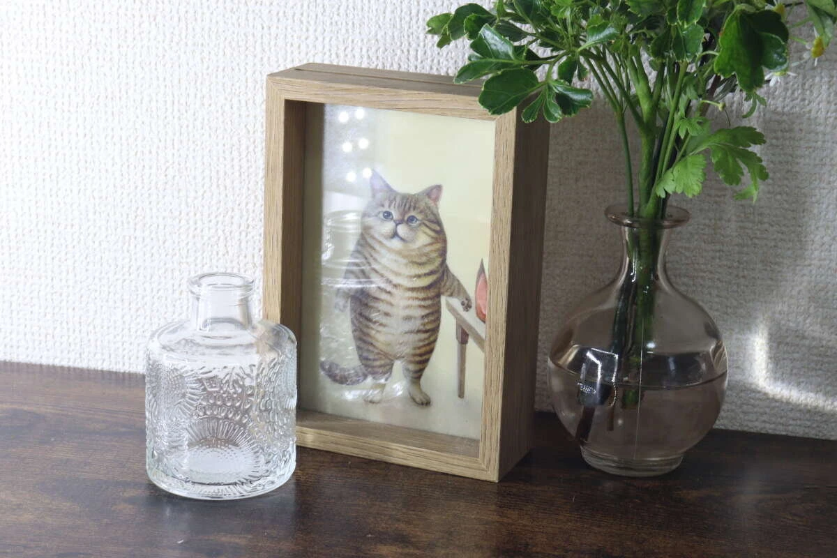 猫の写真立ての横に2種類の花瓶と緑の植物が飾られている棚の上 猫の写真立ての横に2種類の花瓶と緑の植物が飾られている棚の上