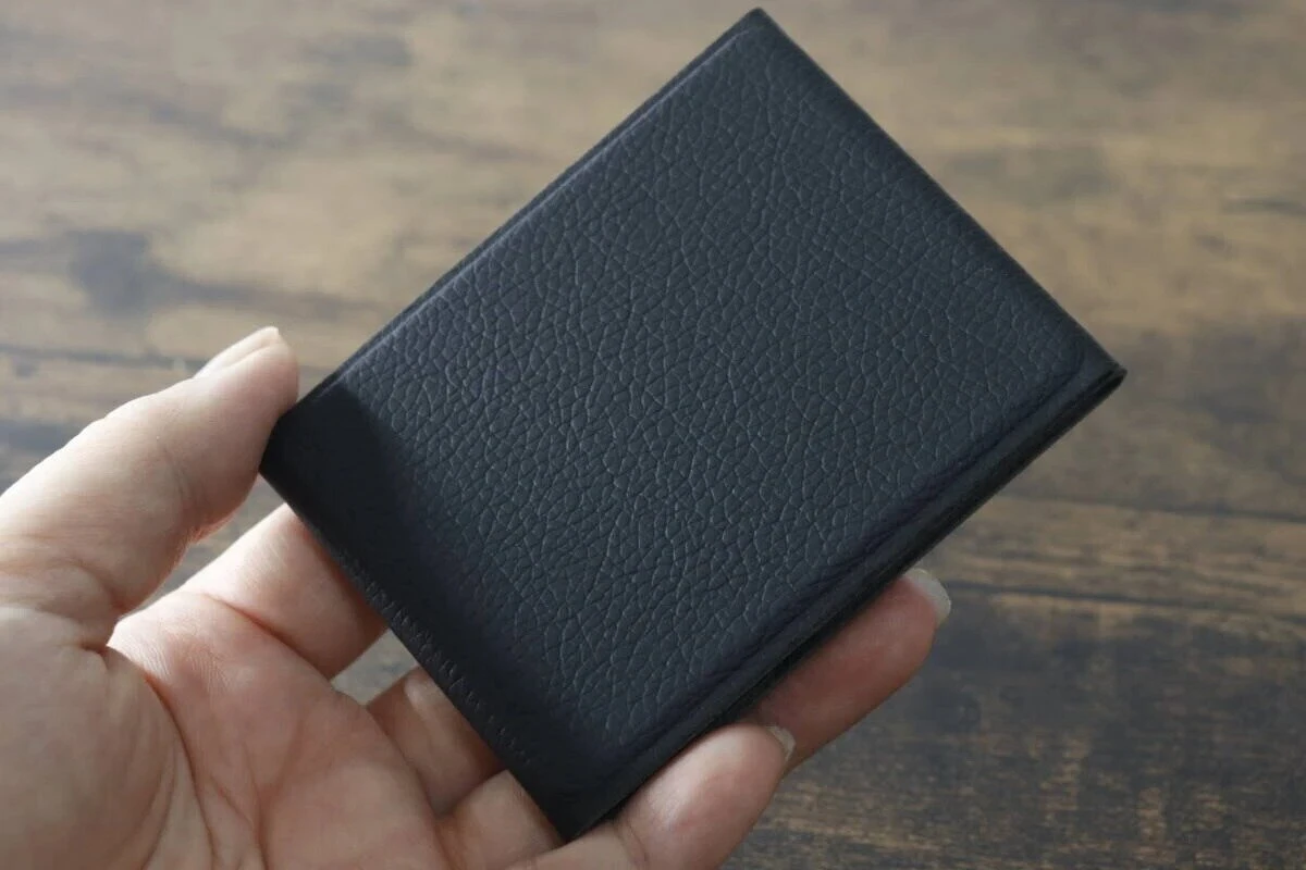 折りたたんだ状態の黒い折りたたみスマホスタンドを手で持っている様子 折りたたんだ状態の黒い折りたたみスマホスタンドを手で持っている様子