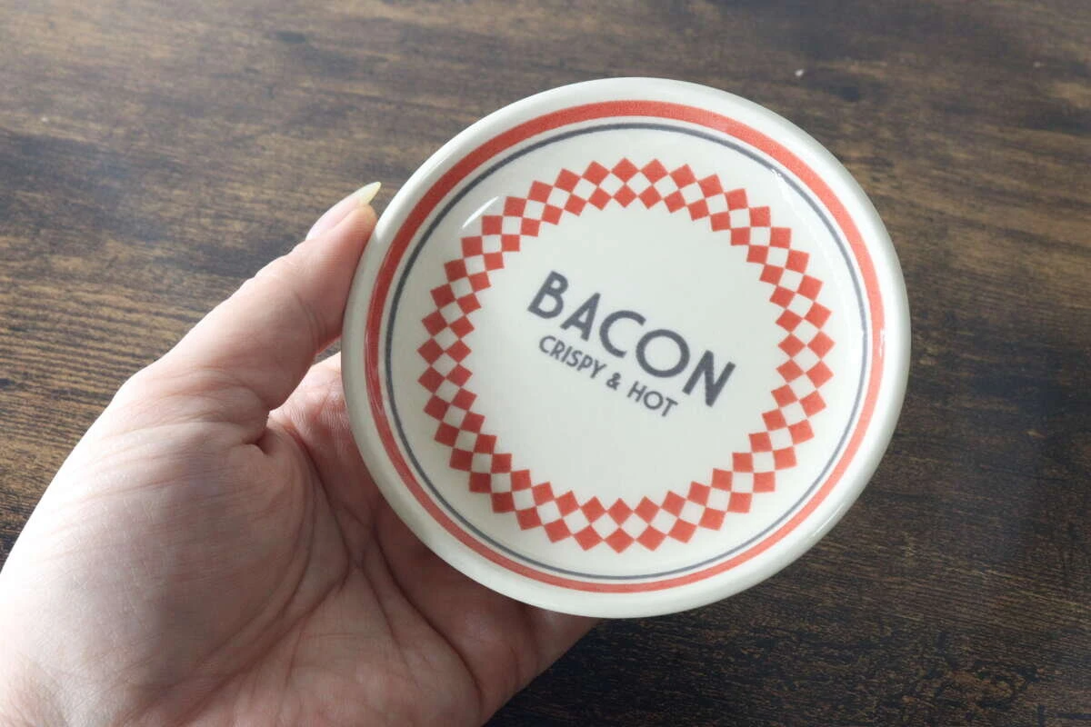 赤いチェック柄とBACONのロゴが入ったMサイズのプレートを手に持っている様子