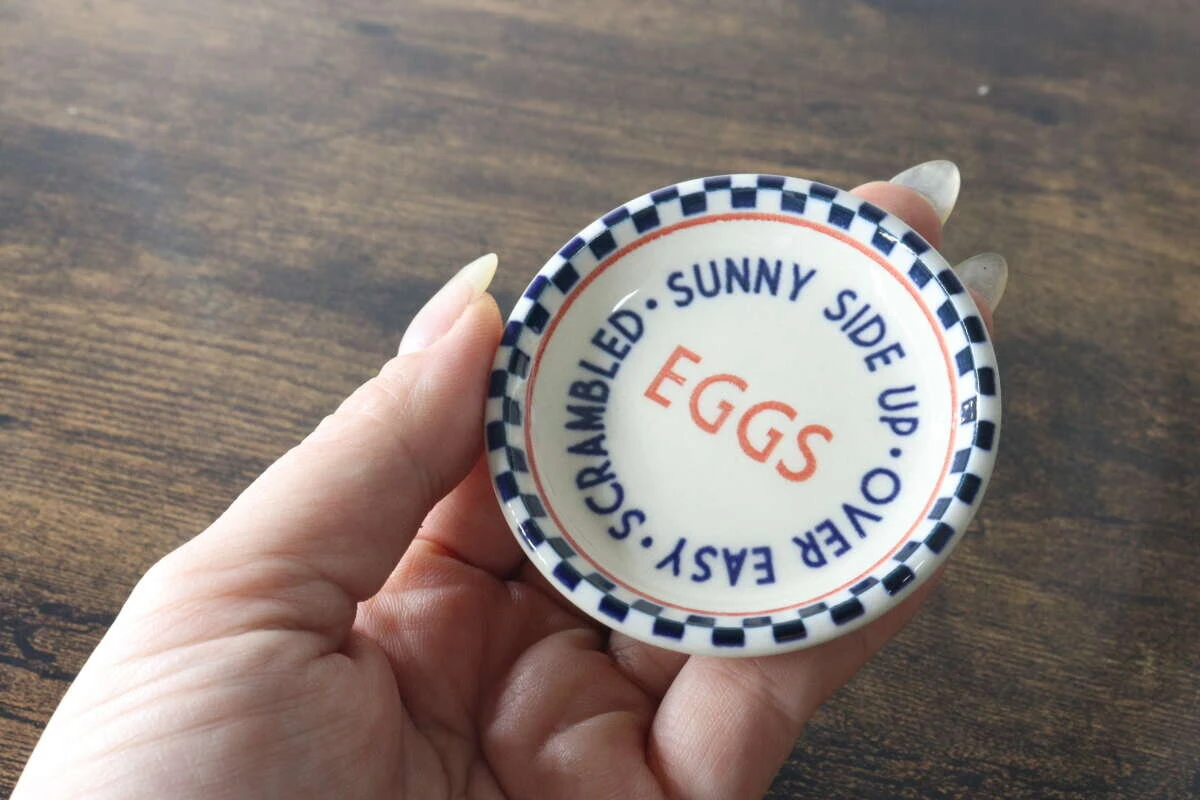 青いチェック柄とEGGSのロゴが入ったSサイズの小皿を手に持っている様子