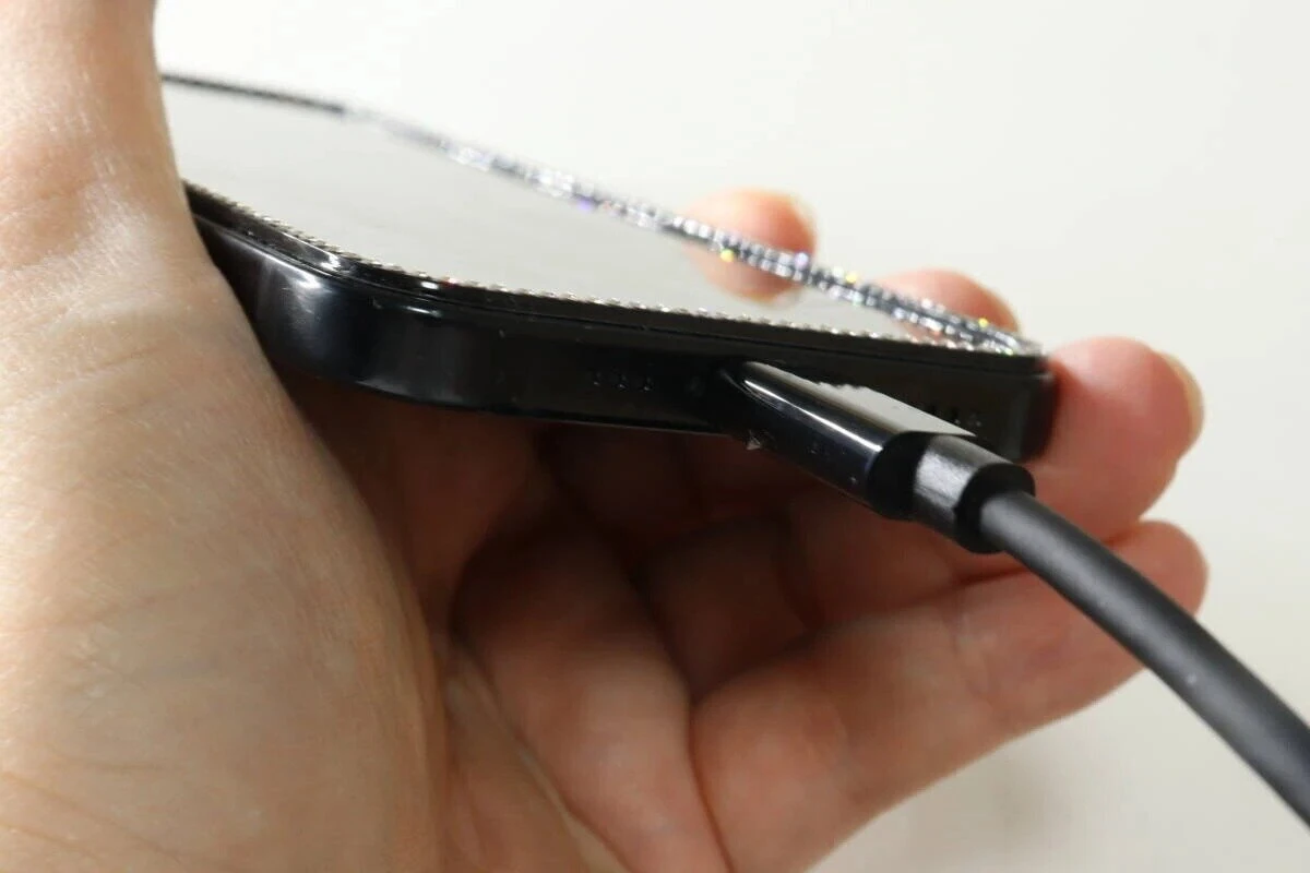 黒いスマホの側面の端子にケーブルを差し込んでいる手元のアップ