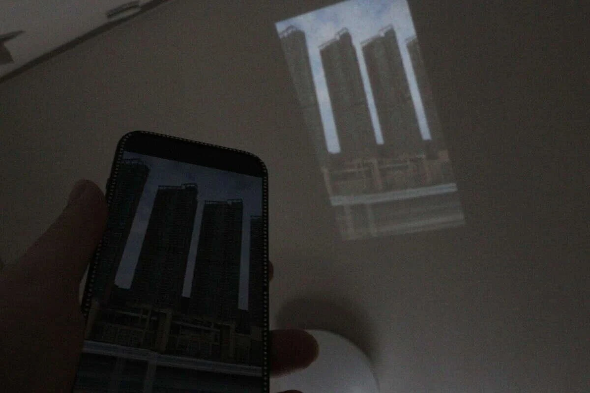 スマホの画面をプロジェクターで壁に投影している暗い部屋の様子