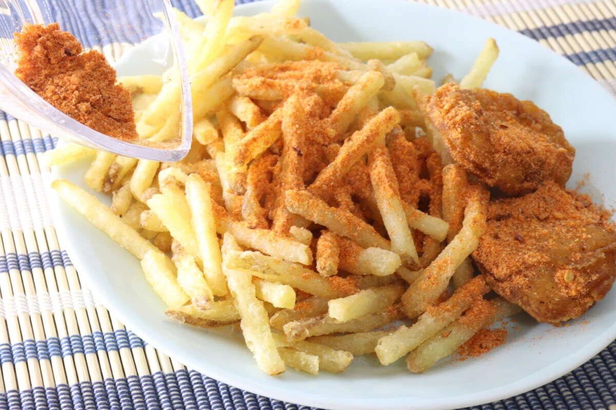 お皿に盛ったフライドポテトとチキンにスパイスをかけている様子