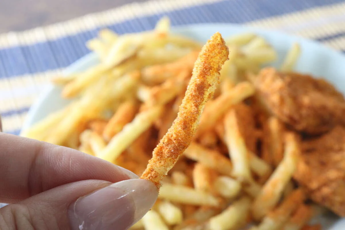 スパイスがしっかりとまぶされたフライドポテトを指で持っている様子