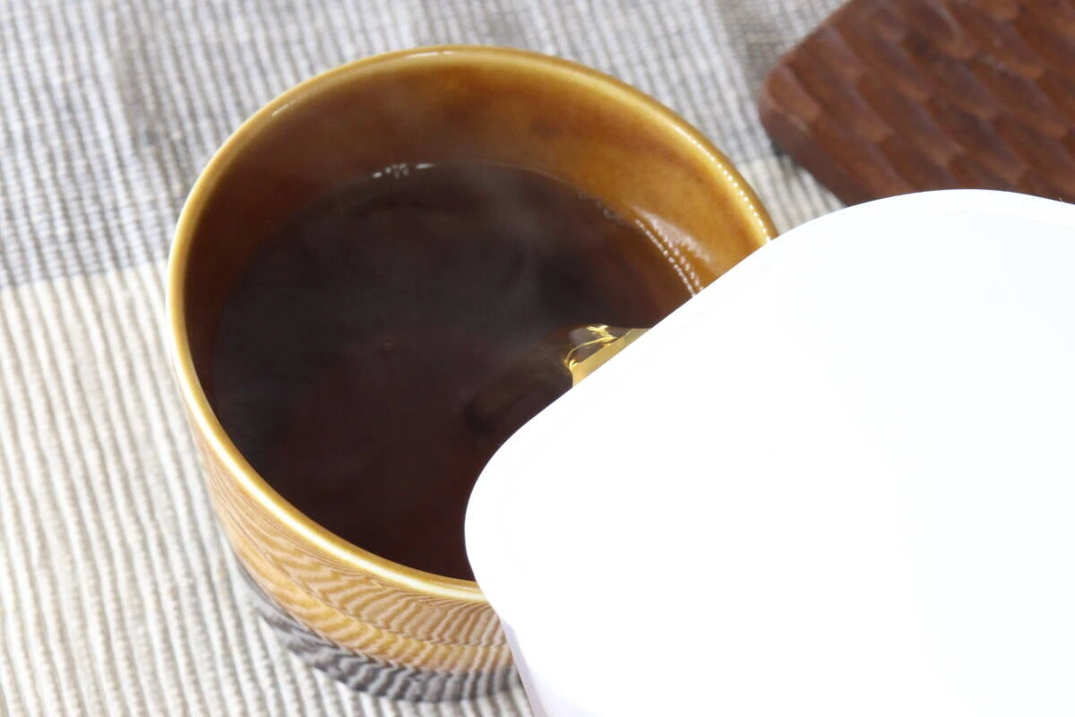 ウォーターポットから茶色いお茶をマグカップに注いでいる瞬間 ウォーターポットから茶色いお茶をマグカップに注いでいる瞬間