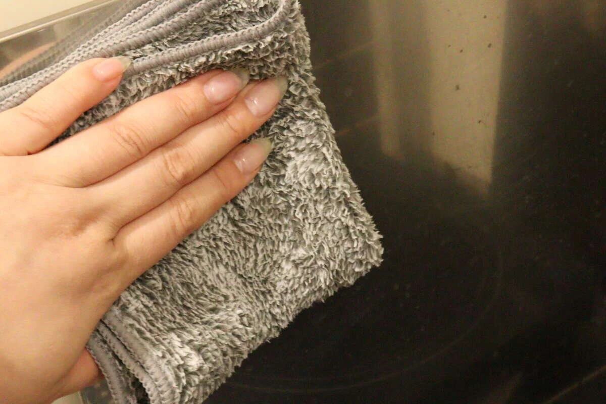 水で濡らした炭配合繊維ふきんでコンロ周りの油汚れを拭き上げている様子