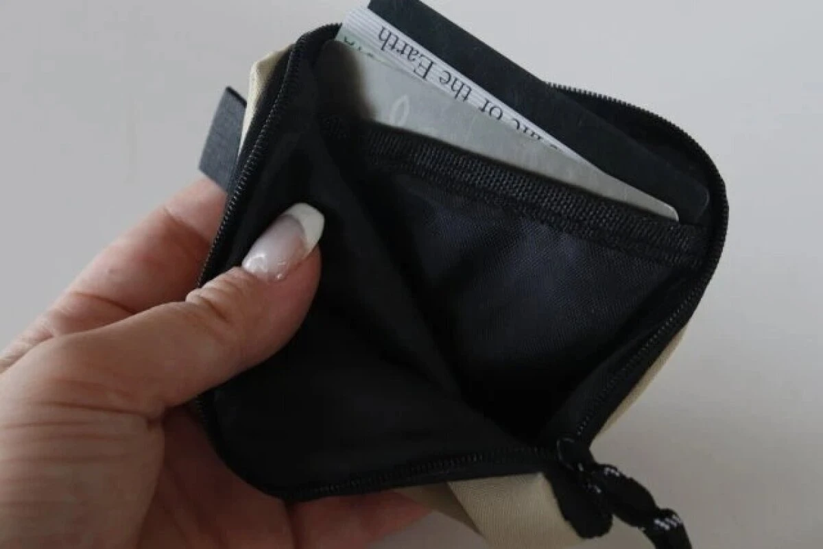 女性がベージュのコインケースのファスナーを開け、中にカードが数枚入っている 女性がベージュのコインケースのファスナーを開け、中にカードが数枚入っている