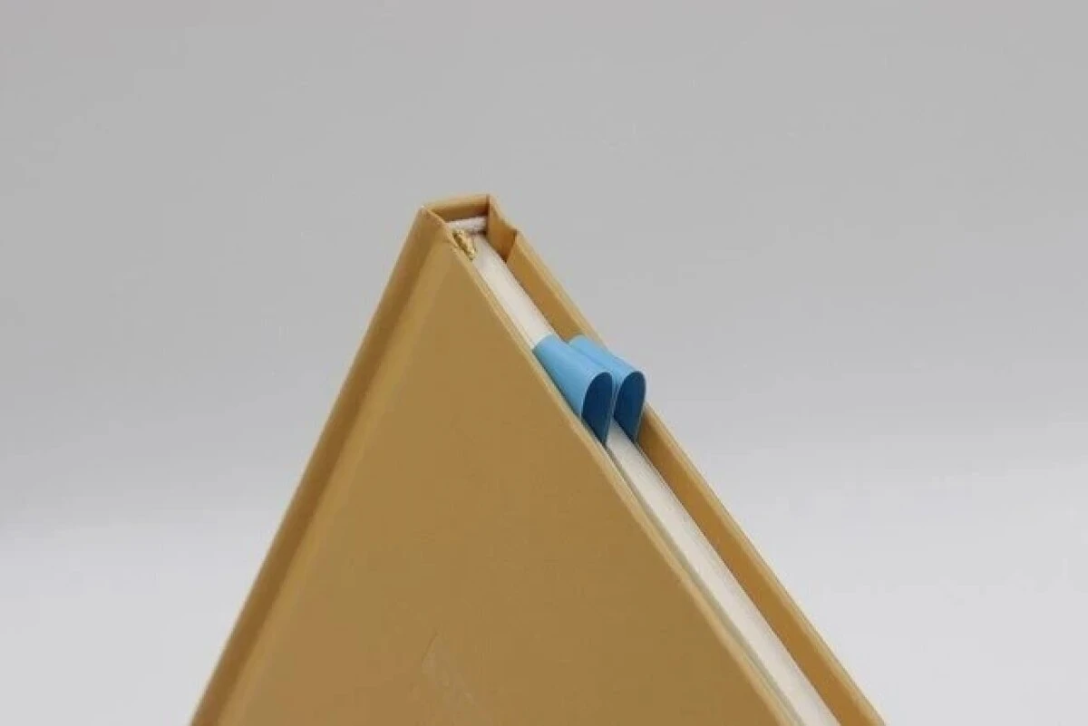 閉じられた茶色いノートの背表紙から、青いサメのしおりが飛び出している 閉じられた茶色いノートの背表紙から、青いサメのしおりが飛び出している