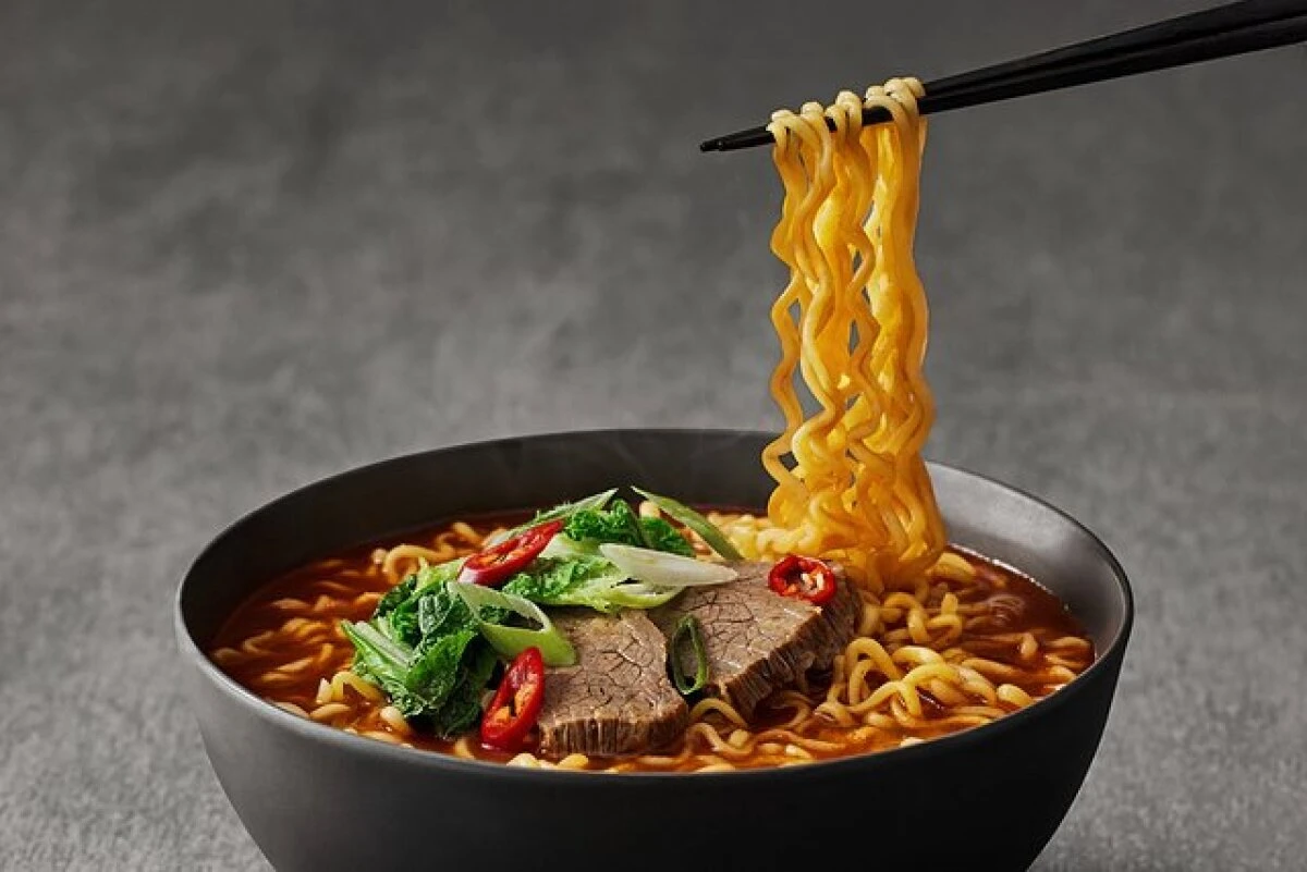 黒い器に入った三養1963ラーメン。箸で麺を持ち上げ、牛肉や野菜が乗っている 黒い器に入った三養1963ラーメン。箸で麺を持ち上げ、牛肉や野菜が乗っている