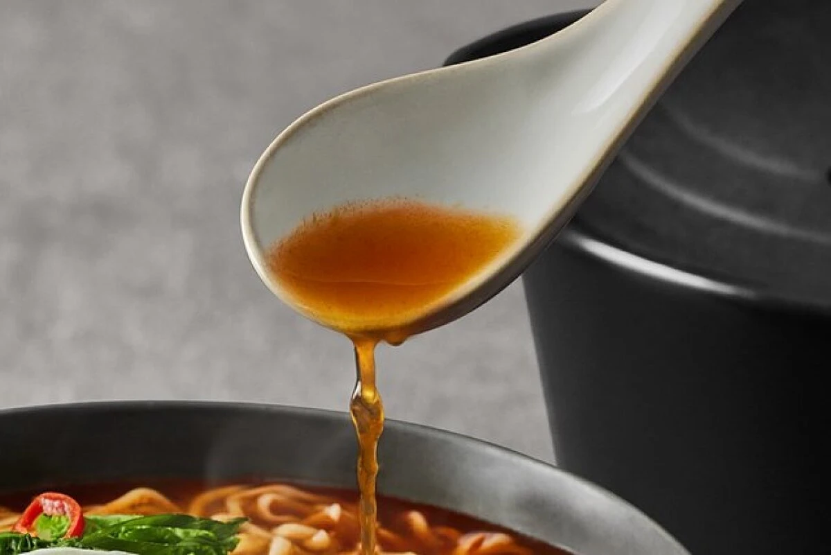 黒い器のラーメンから白いレンゲでスープをすくい、とろりと垂れている様子 黒い器のラーメンから白いレンゲでスープをすくい、とろりと垂れている様子