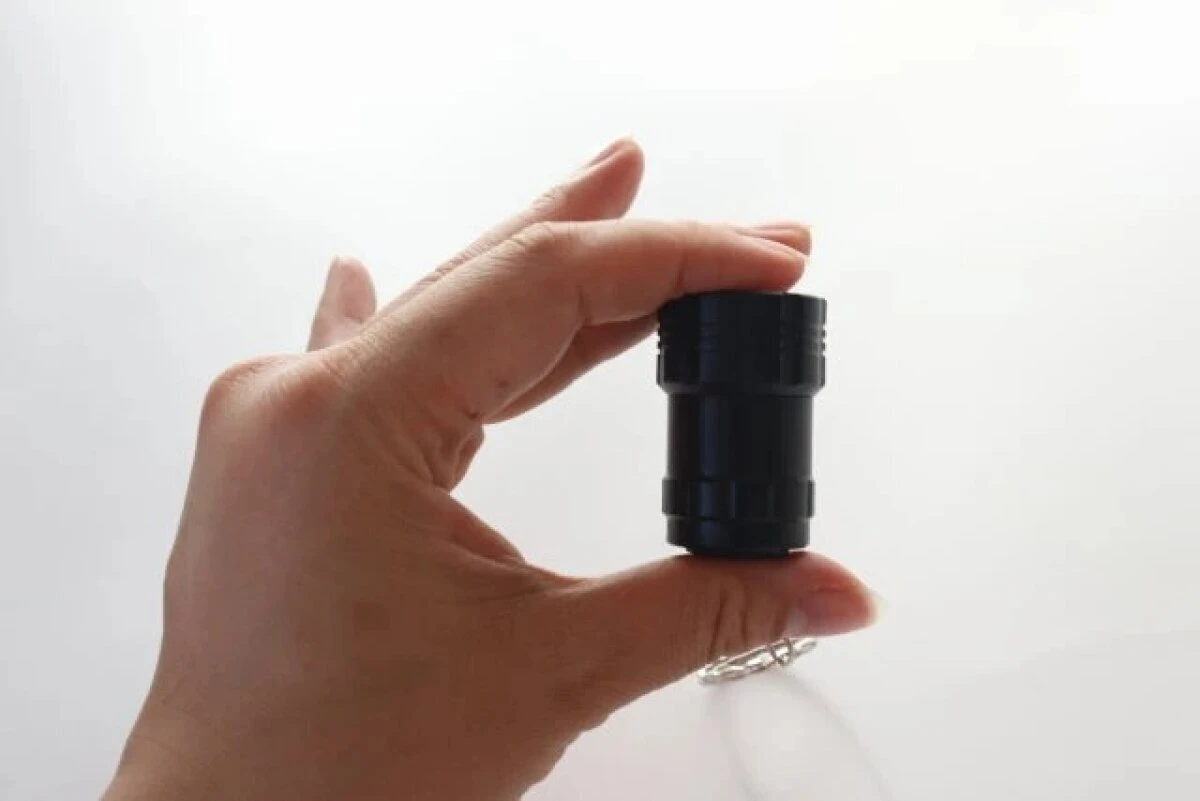 右手が黒い筒状のキーホルダーライトを指でつまんで持っている 右手が黒い筒状のキーホルダーライトを指でつまんで持っている