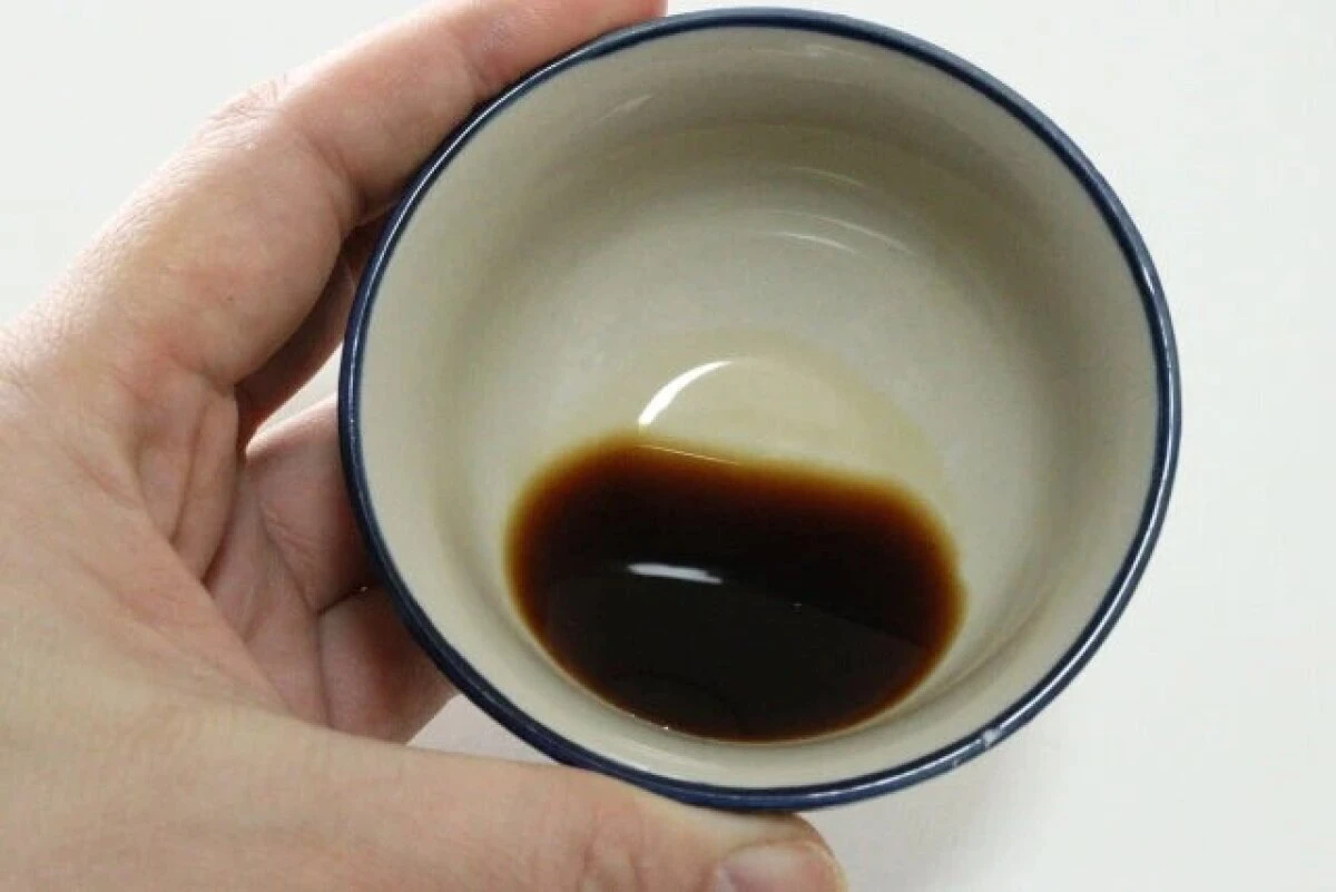 手で持った白い小鉢の底に黒っぽいバルサミコ酢が少量入っている 手で持った白い小鉢の底に黒っぽいバルサミコ酢が少量入っている