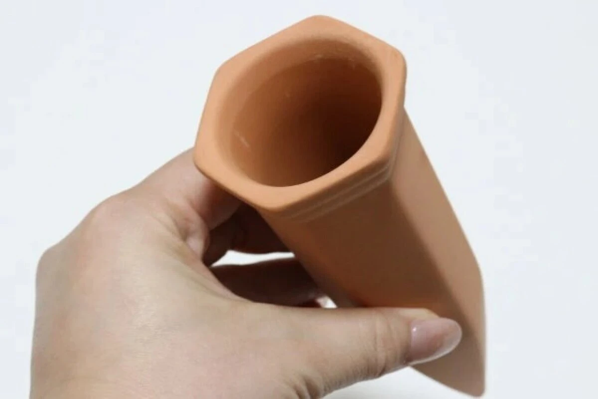 テラコッタ素材で作られた茶色い植物用ウォーターディスペンサーを手に持っている様子