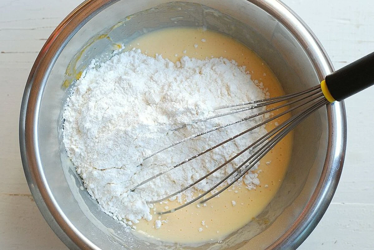 ステンレスのボウルに入った生地に泡立て器を合わせホットケーキミックスを加えている工程 ステンレスのボウルに入った生地に泡立て器を合わせホットケーキミックスを加えている工程