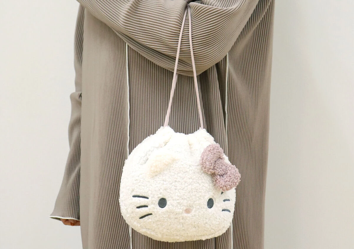 プリーツ素材の服を着た女性がハローキティポーチを肩にかけている